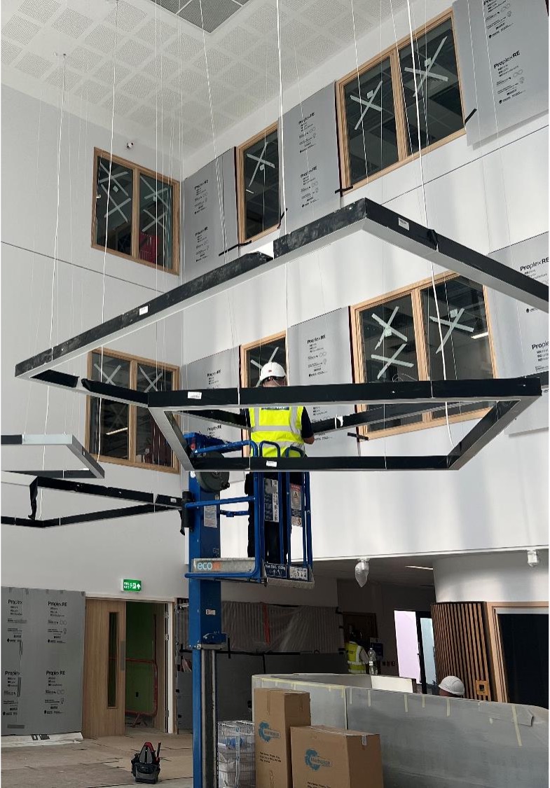A construction worker building a hospital, moving a metal frame into place on a cherry picker